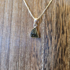 moldavite in a sterling silver setting hanging from a wooden display board