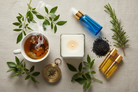 need an image with a white candle in a square glass jar, clear class roller bottles, a steaming cup of tea, black salt, a blue glass spray bottle, an antique compass and surrounded by rue and rosemary