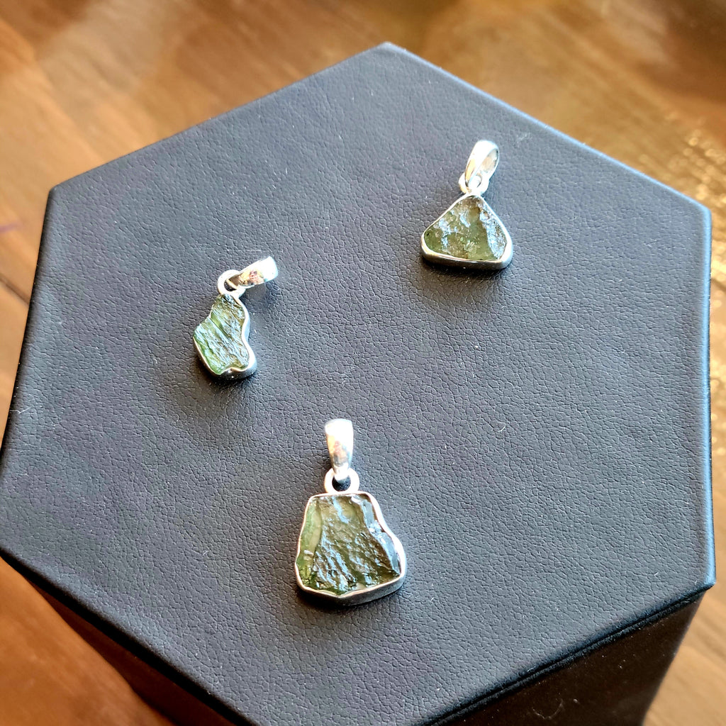 three sterling silver moldavite pendants sitting on a black display