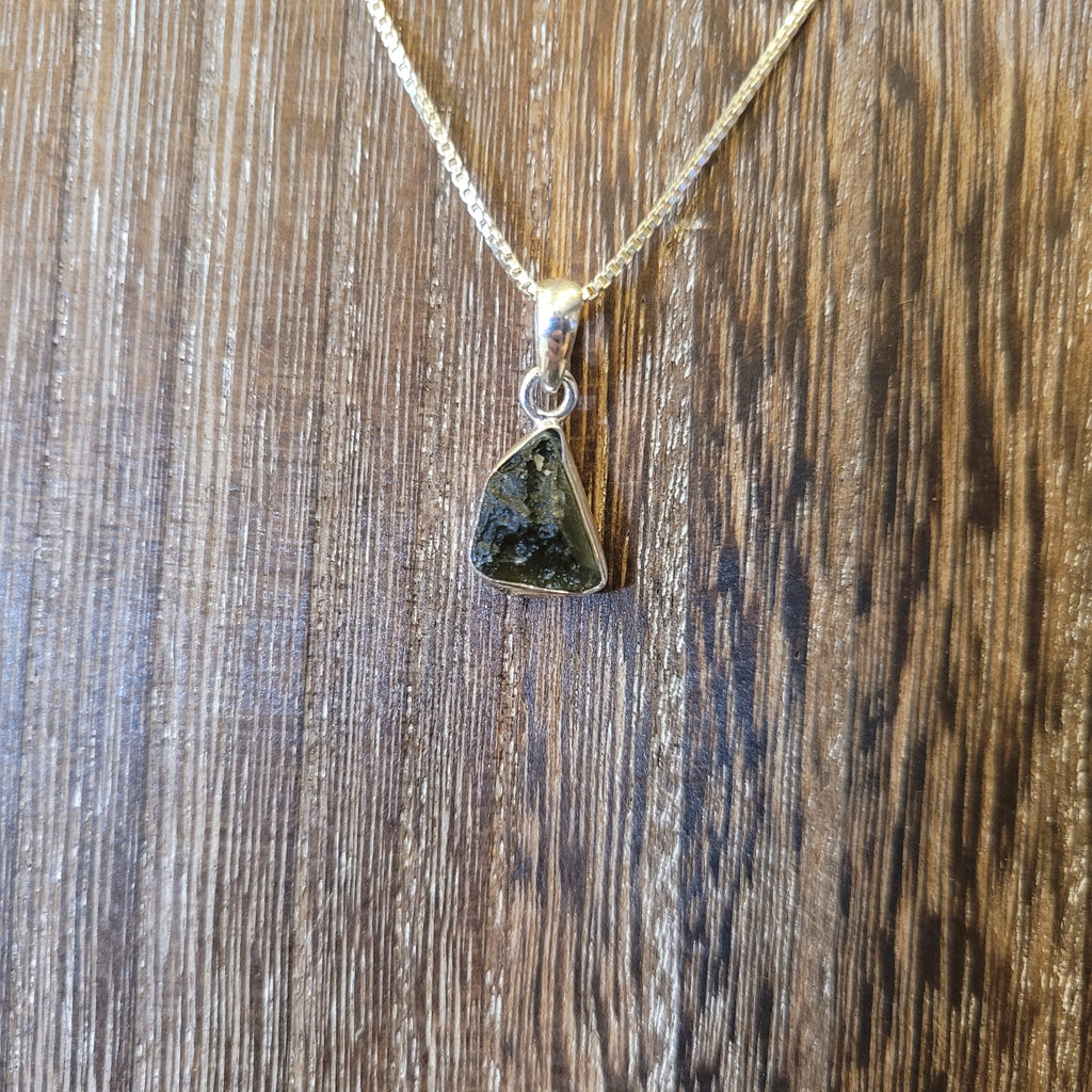 moldavite in a sterling silver setting hanging from a wooden display board